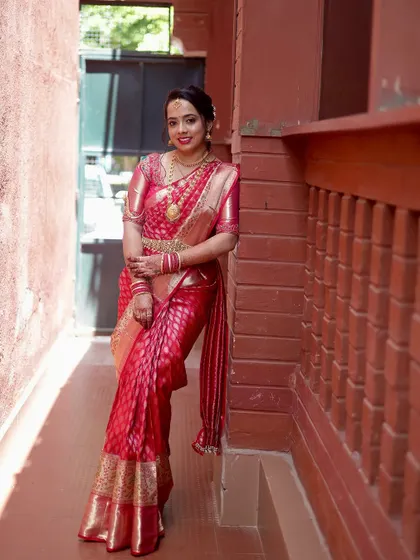 A full-length shot of the bride in a stunning red silk saree. Her makeup is bright and festive, perfect for the celebratory atmosphere of a wedding.