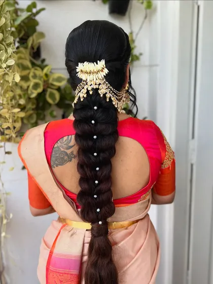 A classic thick braid gets a modern update with a statement hair accessory at the top and delicate pearls placed along its length. The client's tattoo adds a personal touch to the overall look.