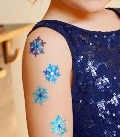 A delicate series of snowflake glitter tattoos on the shoulder. The mix of blue, purple, and silver glitter gives them a lovely icy, wintery feel.