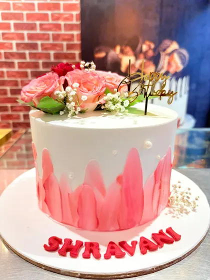 An elegant cake with a pink watercolor effect, topped with fresh roses and baby's breath.