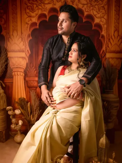 A beautiful maternity portrait of a couple in traditional attire. The studio setup with its warm, earthy tones provides a regal backdrop for this special occasion.
