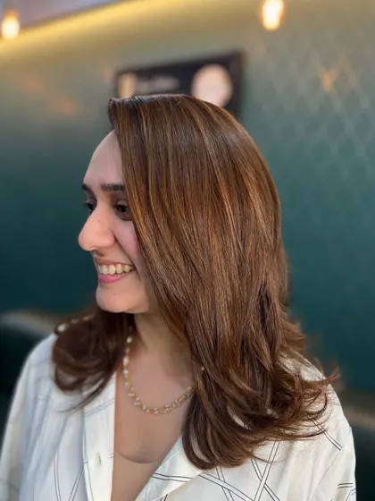 A smiling client showing off her new multi-dimensional brown hair. The color is both sophisticated and vibrant.