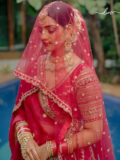 A classic veiled bridal portrait, her eyes closed in a moment of serene contemplation, showcasing her intricate jewelry and makeup.