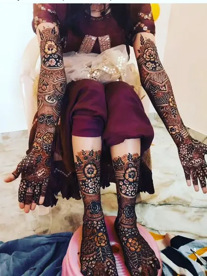 A full-body view of a bride's mehendi, with extensive floral and traditional patterns covering her arms and legs.