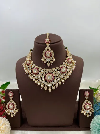 The Zarista Premium Moissanite Necklace set, shown here in both ruby and green variations. This set includes a necklace, maang tikka, and earrings, featuring large central stones surrounded by detailed craftsmanship.