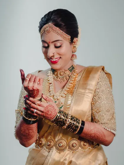 A bride getting ready, wearing a gold Kanchipuram saree. Her custom blouse is fully embroidered with intricate patterns, perfect for her muhurtham look.