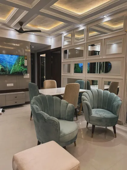 This open-plan living and dining area combines elegance with a welcoming ambiance. We used plush, shell-back accent chairs in a soft teal velvet to add a pop of color, complemented by a mirrored grid wall that enhances the sense of space and light. The design focuses on creating distinct zones for lounging and dining while maintaining a cohesive, luxurious feel.