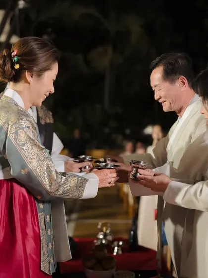 The bride and groom, dressed in traditional Hanbok, share a moment with their family, showcasing the beautiful and intricate attire of the Paebaek ceremony.