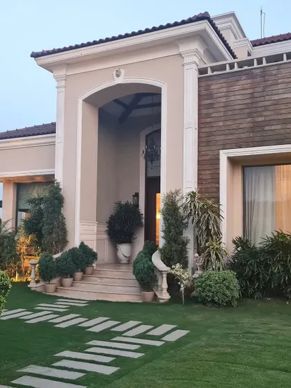 Where textures meet timeless design. This facade blends classic aesthetics like a grand arched entrance with contrasting materials like rustic wood-look tiles, all framed by lush greenery.