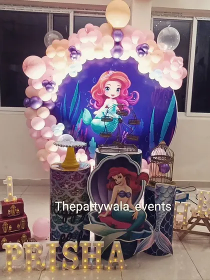 A Little Mermaid theme for a first birthday, featuring a large character backdrop and themed pedestals.