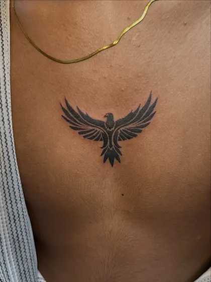 A bold, solid black tribal-style bird tattoo on the back. This minimalist design uses negative space and strong shapes to create a powerful symbol of freedom.