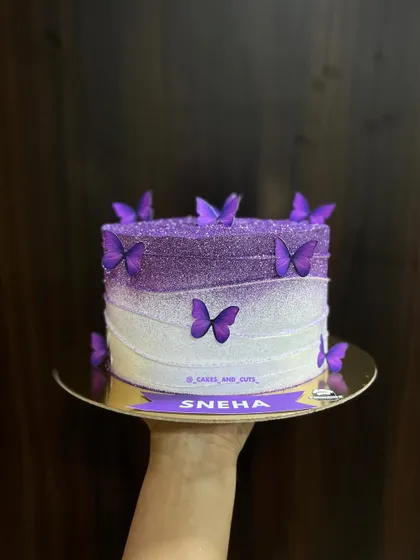 A gorgeous purple ombre cake with glitter and butterflies, personalized with the name "SNEHA". We teach how to achieve this sparkling gradient effect.