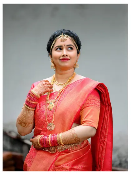 A classic bridal portrait, with the bride looking away thoughtfully, showcasing her elegant red saree and traditional jewelry.