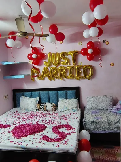 A simple and sweet 'Just Married' room decoration. The bed is covered in rose petals spelling 'I Love You', and the room is filled with red and white balloons to celebrate the new beginning.