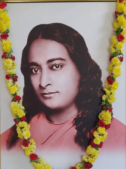 A portrait of our guru, Paramhansa Yogananda, adorned with a garland of yellow flowers and roses. Looking at the master's eyes helps us to feel his living presence and unconditional love.