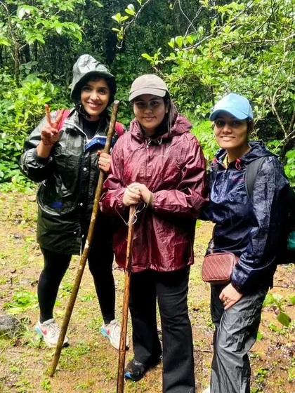 Three team members in rain gear, equipped with trekking poles, smile for a photo on the trail. I ensure everyone is prepared for the weather conditions.