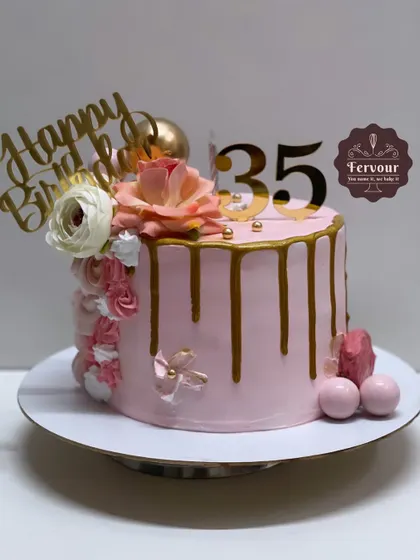 A simple and elegant drip cake for a 35th birthday. The soft pink frosting, gold drip, and floral arrangement create a sophisticated design that is both modern and timeless.