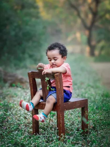 A toddler sits on a small wooden chair in a field of wildflowers, completely absorbed in the tiny leaf he's holding. It’s these quiet moments of discovery that I love to capture.