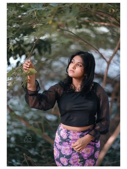 A pensive outdoor portrait, where the subject is interacting with the natural foliage, creating a thoughtful and organic feel.