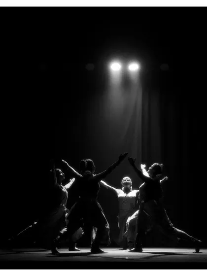 A dramatic black and white silhouette of the ensemble reaching towards the light. This image from "Tyāgarāja Hṛt Sādana" is full of hope and spiritual aspiration.