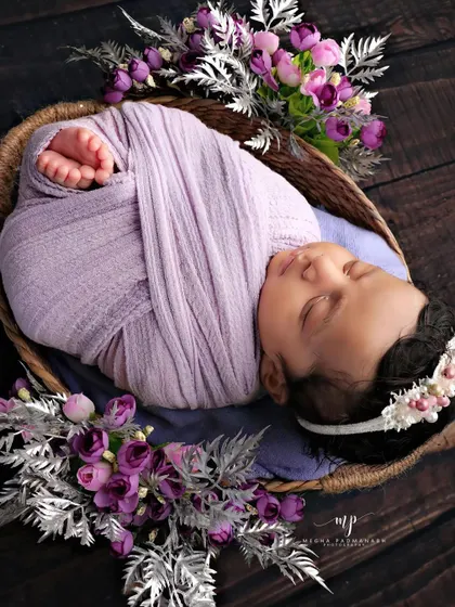 A beautiful composition with a baby in a lavender wrap, surrounded by purple and silver flowers in a dark-toned basket.