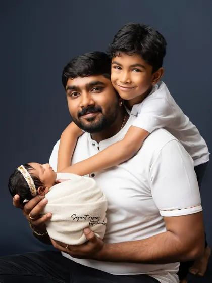 A father proudly holds his newborn while his older son gives him a loving hug from behind. A heartwarming family portrait.