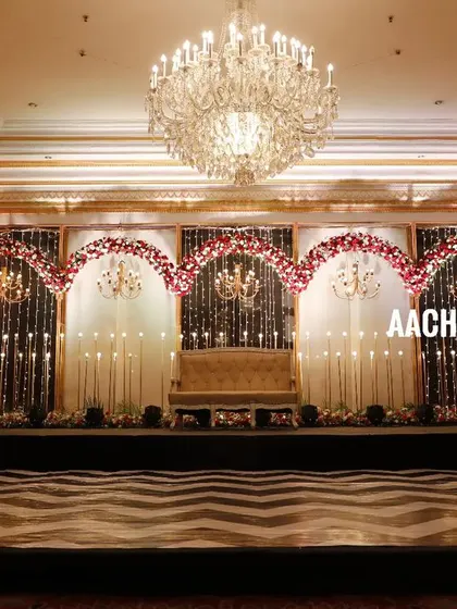 A full view of a grand indoor reception stage with a black and white chevron dance floor. The backdrop features five floral arches with chandeliers, creating a classic and glamorous look for a sangeet or reception night.
