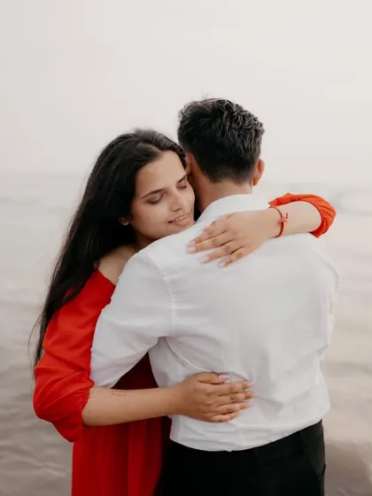 A quiet, intimate moment captured from behind, showing the bride-to-be hugging her partner by the sea. This photo focuses on the feeling of comfort and safety in their embrace.