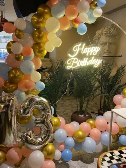 A close-up of the pastel and gold balloon arch for the 13th birthday, complete with a "Happy Birthday" neon sign.