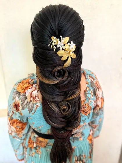 This intricate braid features swirls and rose patterns created from the hair itself, highlighted with a touch of color. A delicate gold accessory completes this artistic hairstyle.
