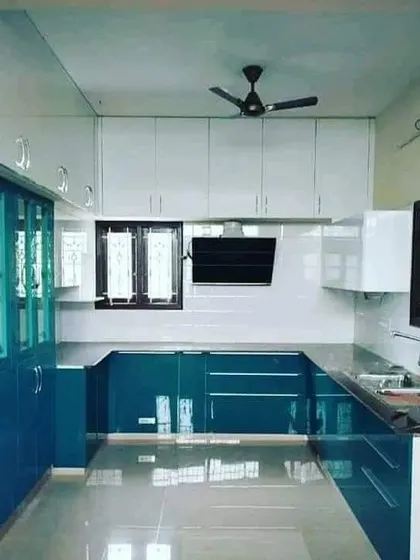 A spacious U-shaped kitchen with glossy teal and white cabinets. The glass-front display cabinets on the side add elegance and storage for crockery.