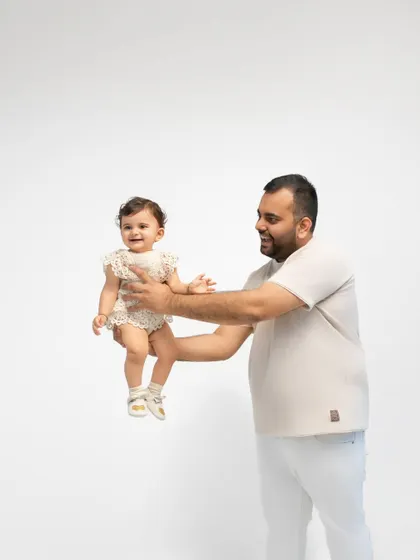 A father holds his daughter, both smiling happily. The clean, minimalist background ensures their bond is the central focus of the image.