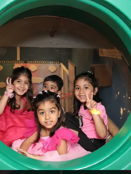 A group of friends peek out from a tunnel in the play structure, sharing a fun moment.