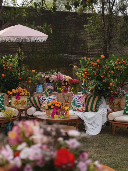 A vibrant Mehendi celebration in a garden, with cozy seating areas surrounded by orange trees and colorful floral arrangements.