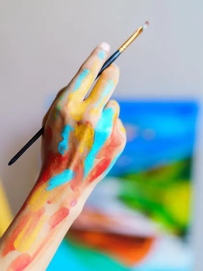 My paint-covered hand holding a brush. This image perfectly captures my philosophy: art is a hands-on, sometimes messy, but always joyful process.