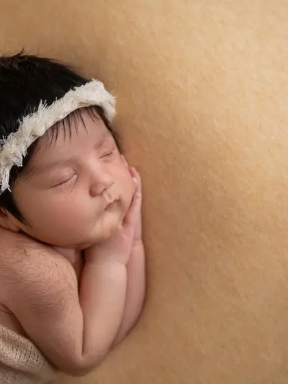 A close up of the baby's face, showing the delicate texture of the white lace headband against her dark hair.