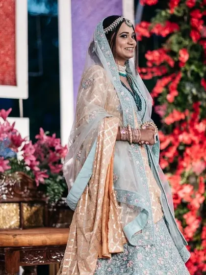 The bride smiles during her pre-wedding ceremony. The backdrop of red and pink flowers adds a rich and celebratory feel to the occasion.