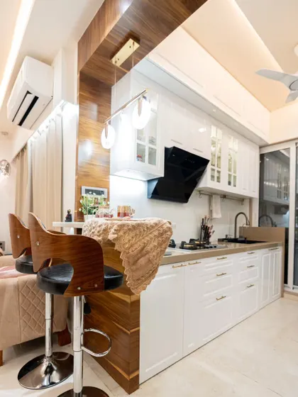 An open kitchen concept that connects the cooking area with the living room. This design features classic white shaker-style cabinets, a breakfast bar with stylish high chairs, and warm wood accents for a cozy, inviting feel.