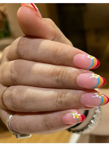 Taste the rainbow with these colorful nails. This design features a rainbow-striped French tip on a sheer base, accented with a tiny, cute daisy on each nail.