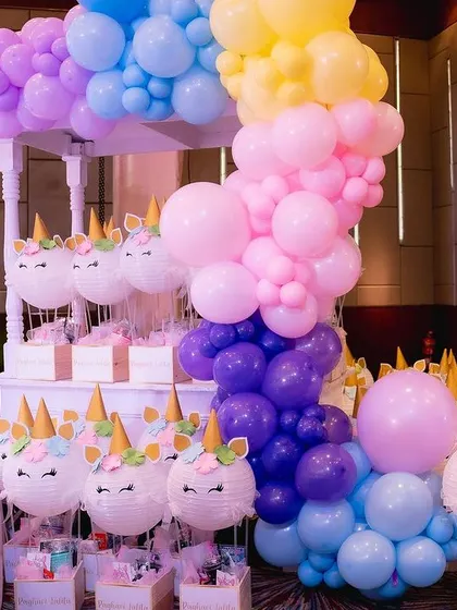 A rainbow of balloons cascades down from a custom-built stand holding unicorn-themed party favors.