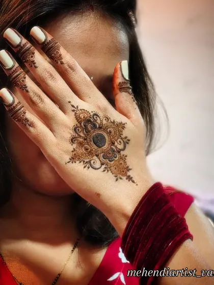 A posed shot showing off the beautiful mandala mehendi on the back of the hand, complemented by red bangles.
