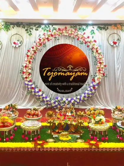 A wide view of an ear piercing ceremony setup, with a floral wreath backdrop and a neat arrangement of traditional plates.