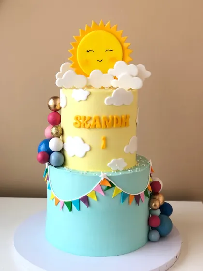A cheerful "You Are My Sunshine" themed two-tiered cake, with a happy sun topper and colorful bunting.