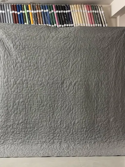 The solid grey backing of the quilt, which highlights the leaf-and-vine quilting pattern.