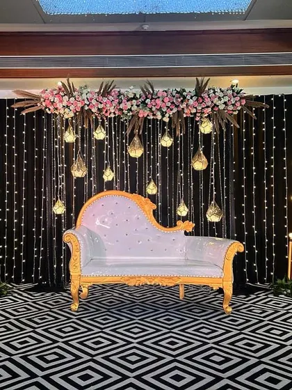 This Sangeet stage combines a black fairy light backdrop with modern geometric flooring. The design is clean and contemporary, with hanging glass terrariums and a floral-topped couch for the couple.