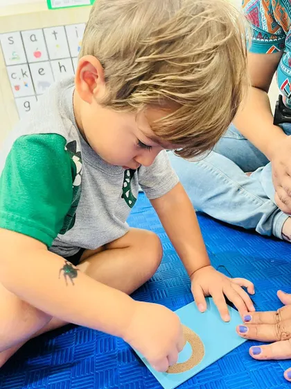 A boy carefully traces a sandpaper number "0," learning about the concept of zero and its shape through touch.