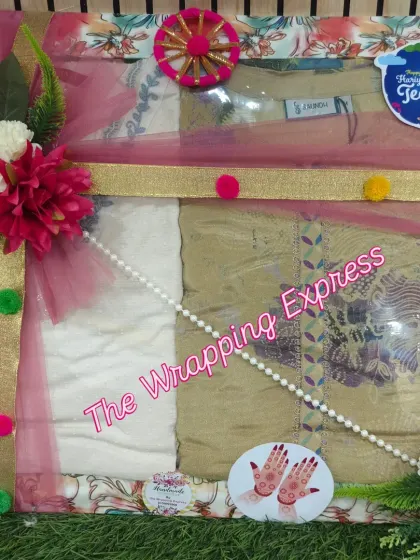 A beautifully packed suit for Teej, decorated with pink net, a golden ribbon, and traditional 'jhula' and 'mehndi' cutouts.