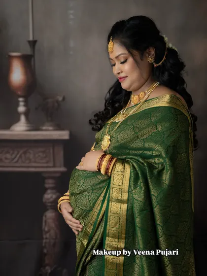 A classic maternity photoshoot portrait. The rich green saree and traditional gold jewelry create a timeless and regal look for this mom-to-be.