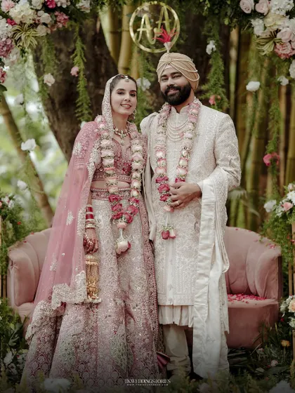 A classic portrait of a Punjabi couple in their wedding attire, set against a beautiful floral and bamboo backdrop.