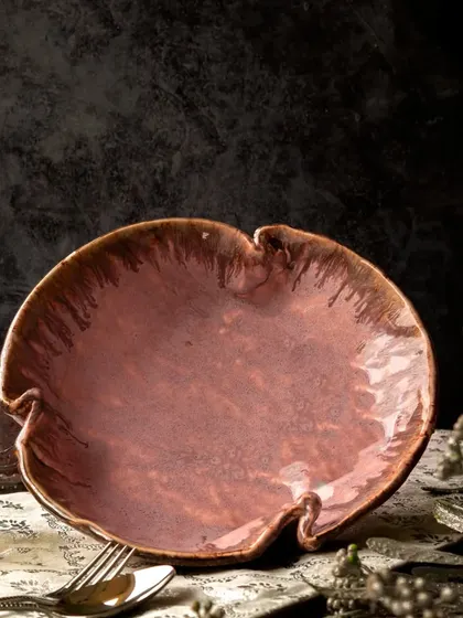 The empty burgundy bowl is the star of this moody, atmospheric shot. The dramatic lighting and dark background highlight its unique, organic shape and rich, textured glaze.